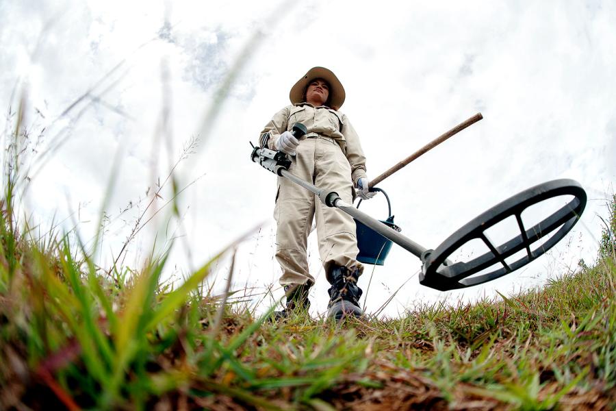 A deminer searching for UXO with a metal detector.
